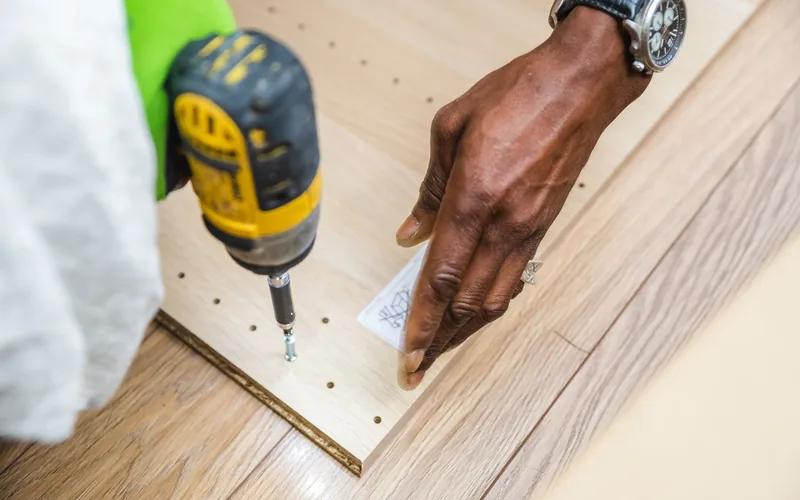 Behandschuhte Hand setzt mit dem Akkuschrauber eine Schraube in eine frisch verlegte Bodendiele
