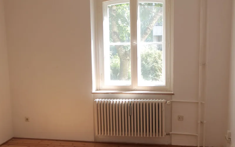 Leer geräumtes Zimmer mit Dielenboden, Heizkörper und Fenster, nichts steht mehr darin